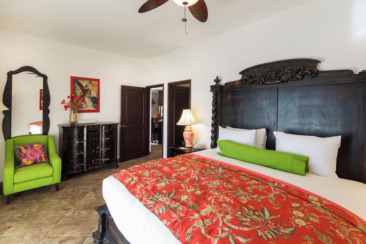 A bedroom with a large bed, a green armchair, a dresser, and a ceiling fan.