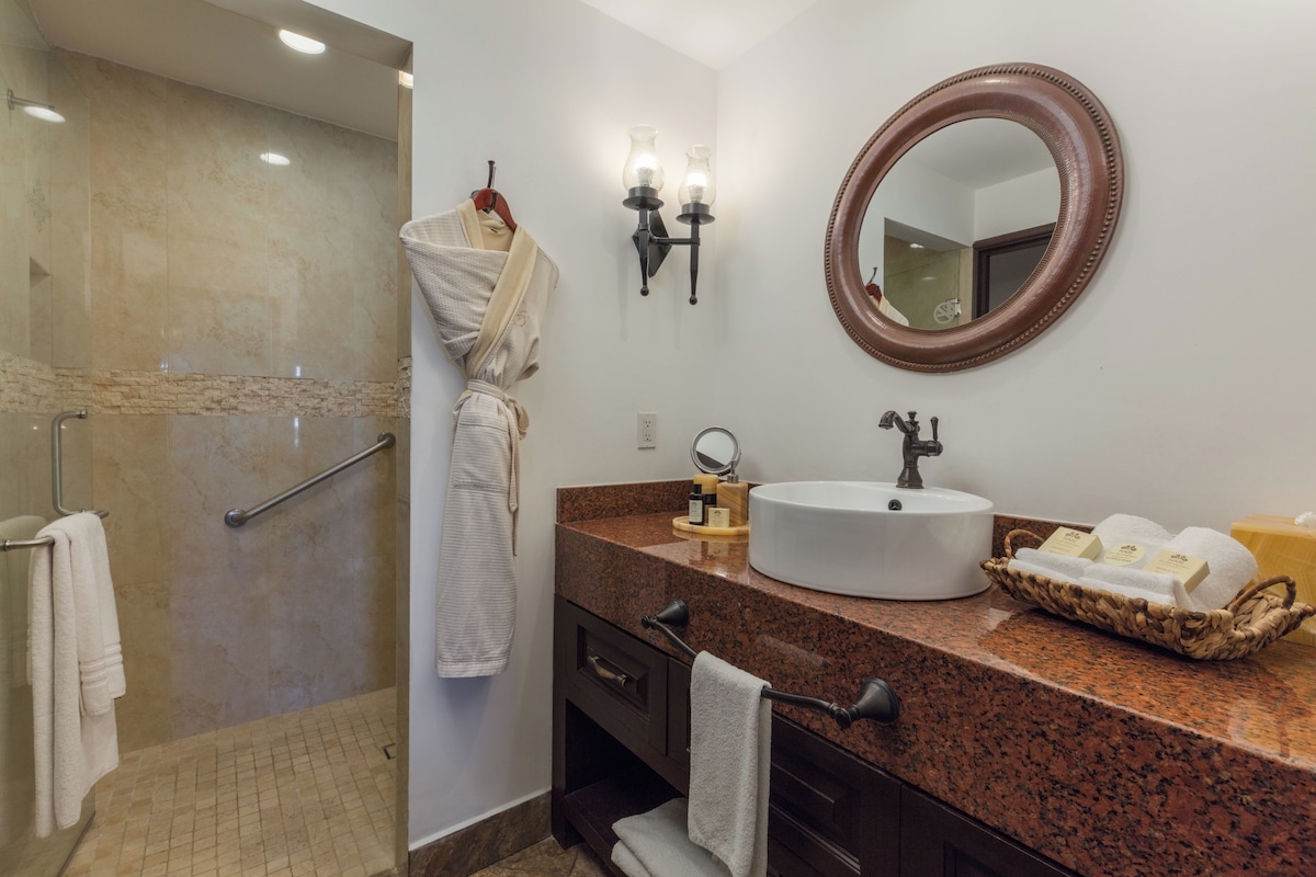 A bathroom with a granite countertop, a sink, a mirror, and a shower area.