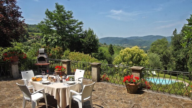 An outdoor dining area with a stone table, white chairs, and a view of a pool and mountains. - Villa Lucolena - Villa with private pool (Lucolena In Chianti)