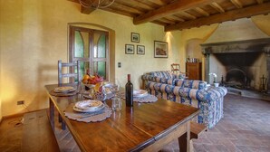 A dining area with a wooden table set for a meal, a floral sofa, and a fireplace in the background. - Villa Lucolena - Villa with private pool (Lucolena In Chianti)