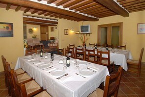 Un espace repas avec plusieurs tables dressées pour le repas, des chaises en bois et un téléviseur fixé au mur.