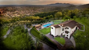 Ett flygbildsfoto av en villa med en swimmingpool, omgiven av frodig grönska och med utsikt över en avlägsen stad.