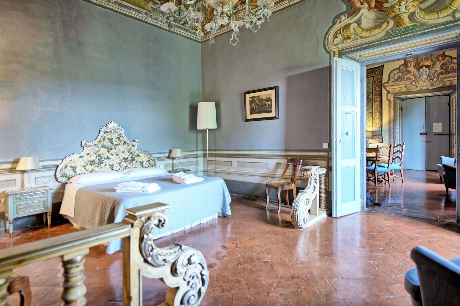 Een ruime kamer met een groot bed, decoratief meubilair en een kroonluchter.
