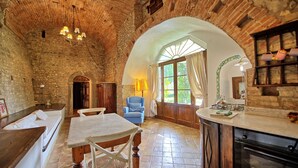 A rustic kitchen with a stone wall, wooden furniture, and a large window. - Bastione - Apartment with swimming pool (Montegufoni)
