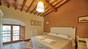 A bedroom with a large bed, a wooden ceiling, a radiator, and framed pictures on the wall.
