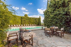A poolside area with lounge chairs and a table set for dining, surrounded by lush greenery.