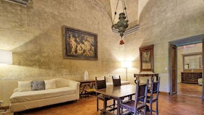 A spacious room with a large painting on the wall, a dining table with chairs, a sofa, and a lamp.