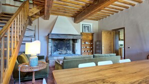 Un intérieur rustique agrémenté d’une cheminée, de poutres en bois, d’un escalier et d’un coin repas.