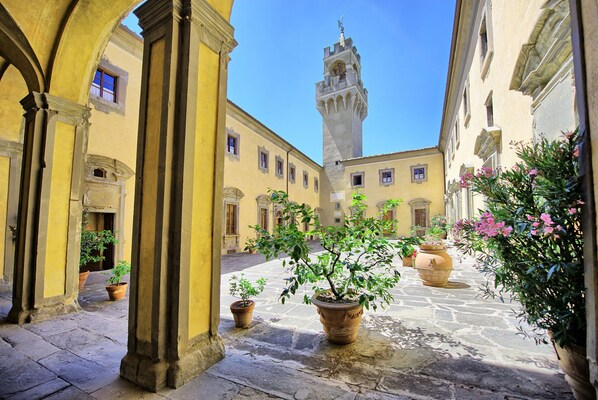 A courtyard with yellow buildings, a tower, and potted plants.