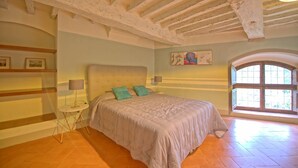 A bedroom with a large bed, a small table, a lamp, and a painting on the wall.