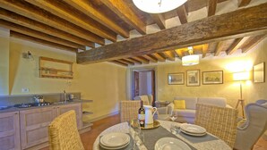 A dining area with a wooden ceiling, a kitchen with a gas stove, wicker furniture, and a table set for two with plates and a bottle.