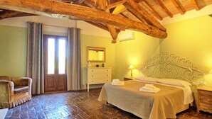 Une pièce comprenant un lit, une chaise, une commode, un miroir et une fenêtre avec des rideaux.