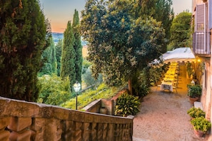 A stone staircase leading to a dining area with tables set for a meal, surrounded by lush greenery and tall trees.