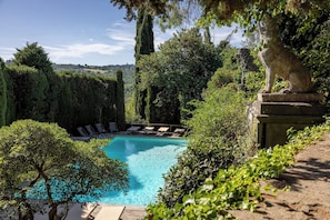 Una piscina rodeada de exuberante vegetación, estatuas de piedra y una vista despejada del paisaje.