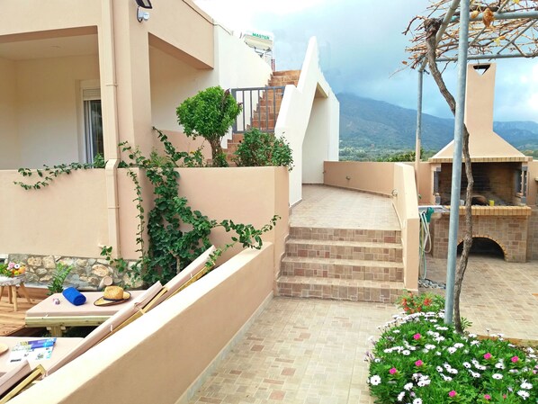 Un balcón con vistas a montañas, zona de barbacoa y un pequeño jardín con flores.