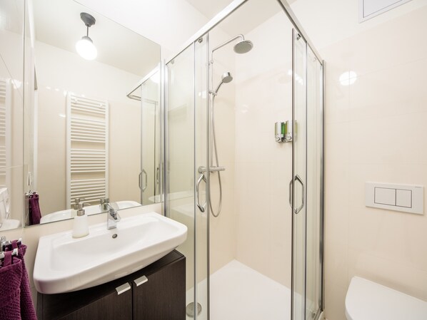 A modern bathroom with a glass-enclosed shower, a white sink, and a toilet.