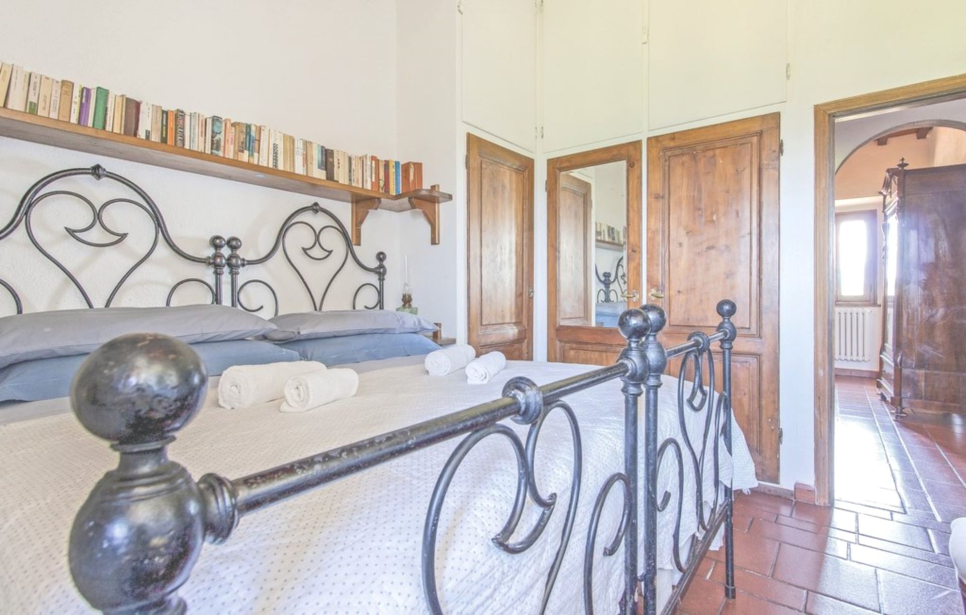 A bedroom with a metal bed frame, a wooden bookshelf, and a large mirror.