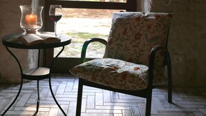 Een kamer met uitzicht op bomen door een raam, een stoel, een tafel met een kaars en een glas rode wijn.