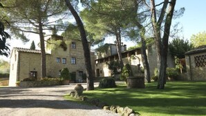 Un bâtiment en pierre avec une allée de gravier, entouré d’arbres et d’une pelouse bien entretenue.
