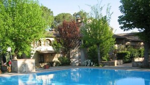 Une piscine à l’eau d’un bleu limpide, entourée de verdure et de structures en pierre.