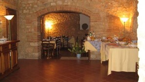 Un espace repas avec des murs en pierre, une arche en briques et des tables dressées pour le repas.