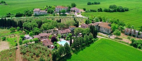An aerial view of a rural property with multiple buildings, a swimming pool, and surrounding green fields.