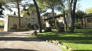 Un edificio de piedra con varias ventanas y un camino de grava que conduce a una zona verde con árboles.