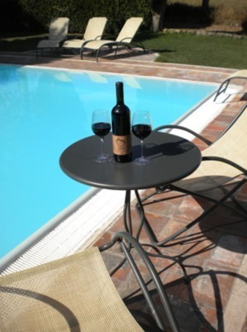 A poolside table with a bottle and glasses, surrounded by lounge chairs.