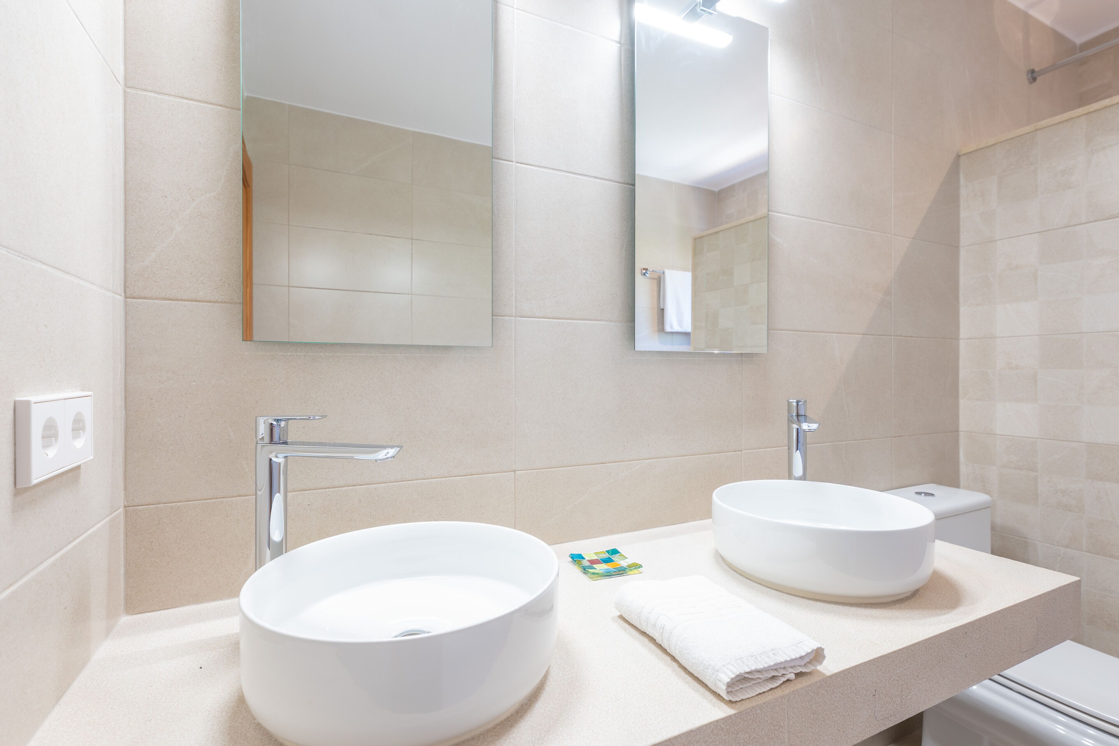 A modern bathroom with two large white sinks, a mirror, and a toilet.