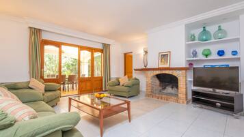 Una sala de estar con un sofá verde, una mesa de centro con fruta, una chimenea y un televisor sobre un mueble.