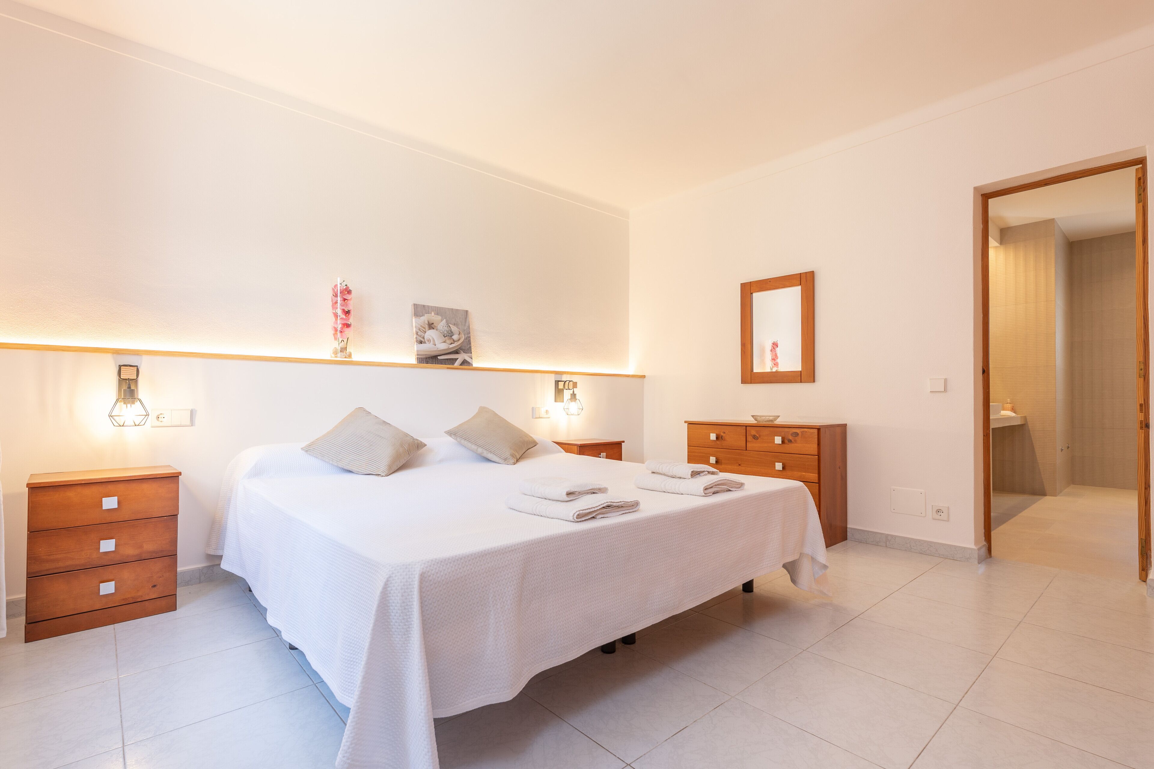 Une chambre à coucher avec un grand lit, des tables de chevet en bois, une commode et un miroir au mur.