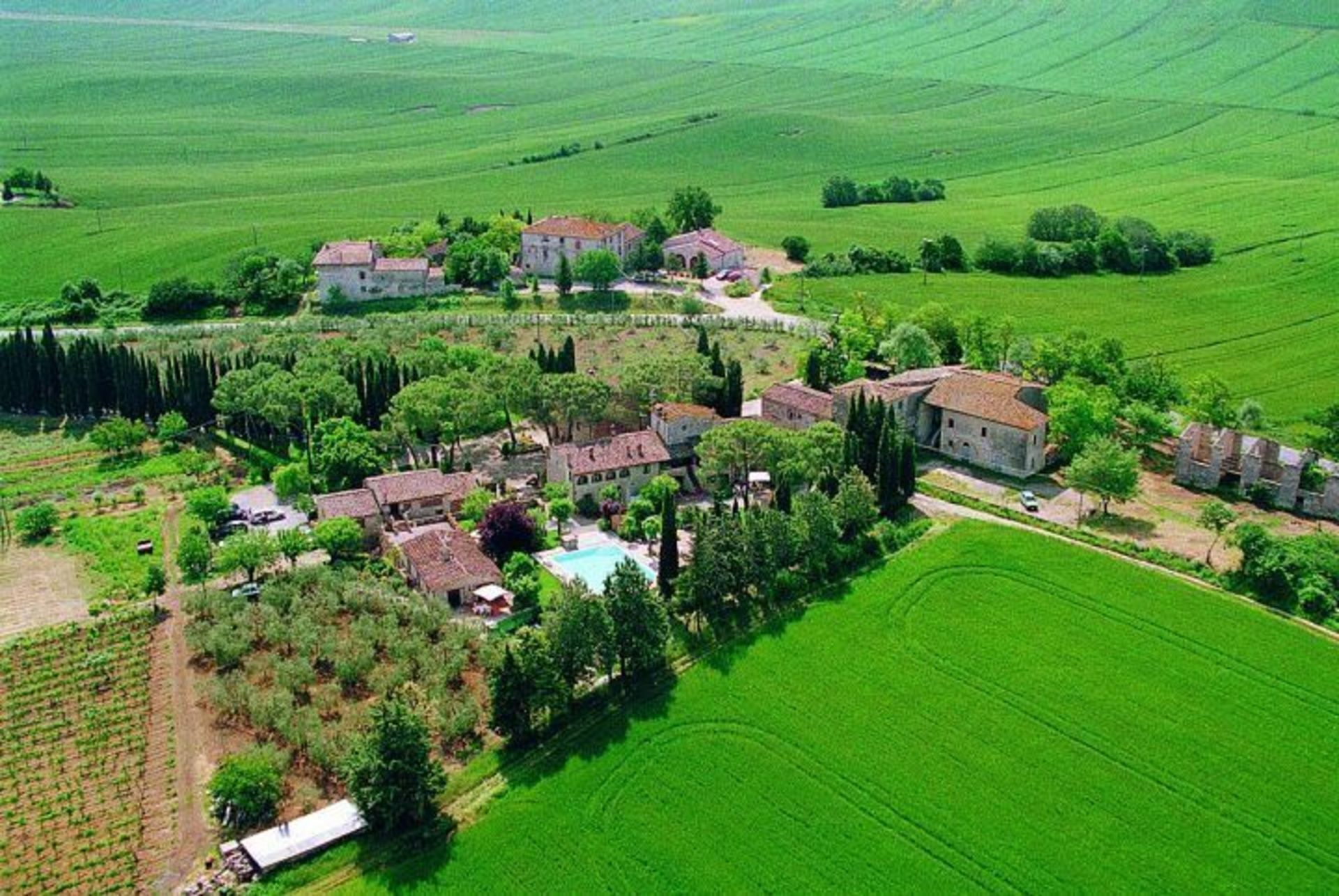 An aerial view of a rural property with multiple buildings, a swimming pool, and surrounding green fields.