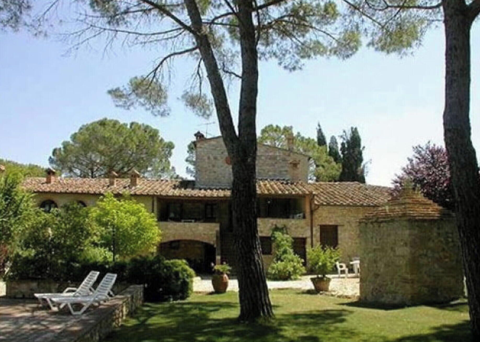 Un edificio in pietra con tetto in tegole, circondato da alberi e un piccolo prato.