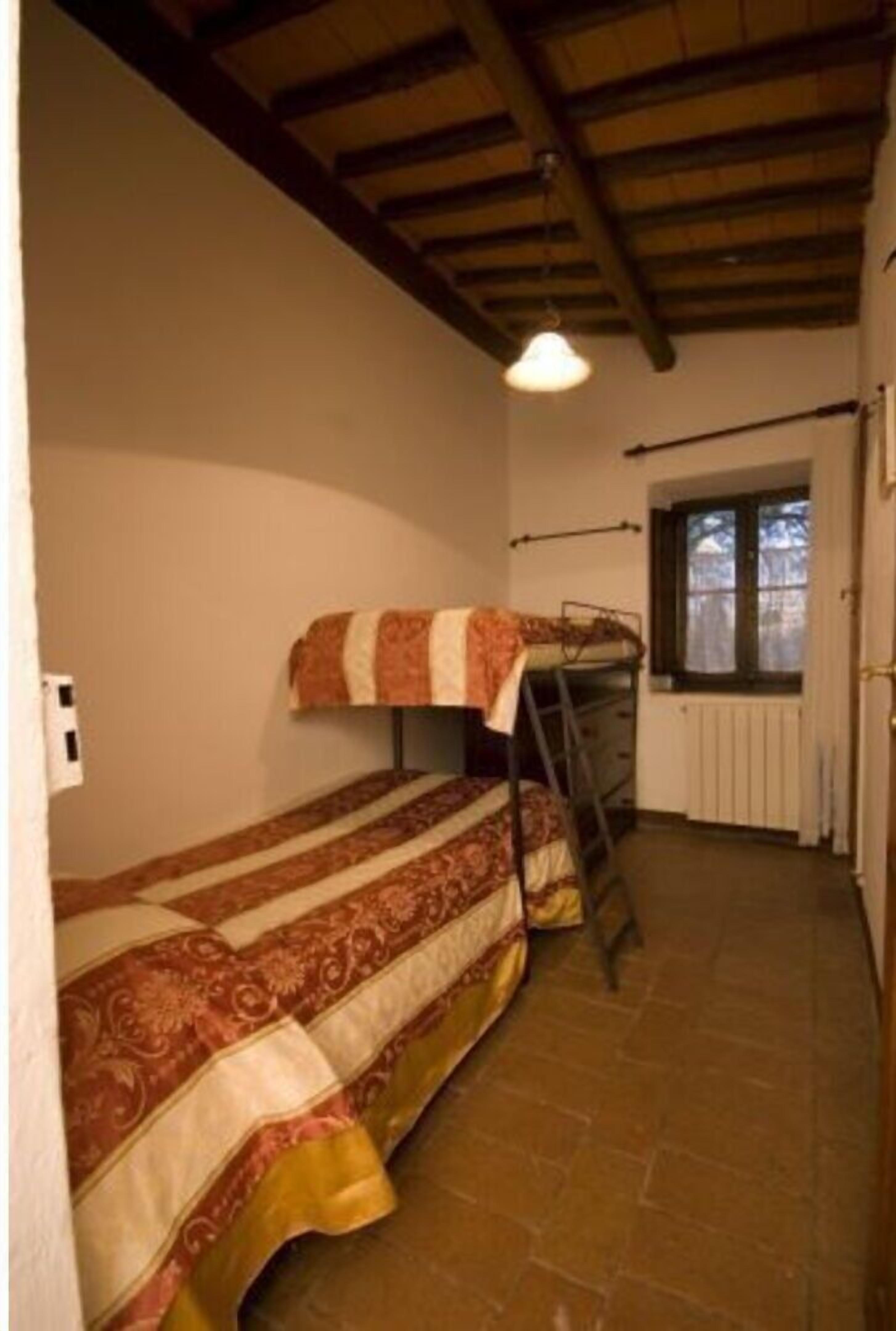 A small, single-room accommodation with a bunk bed, a ladder, a window, and a radiator.