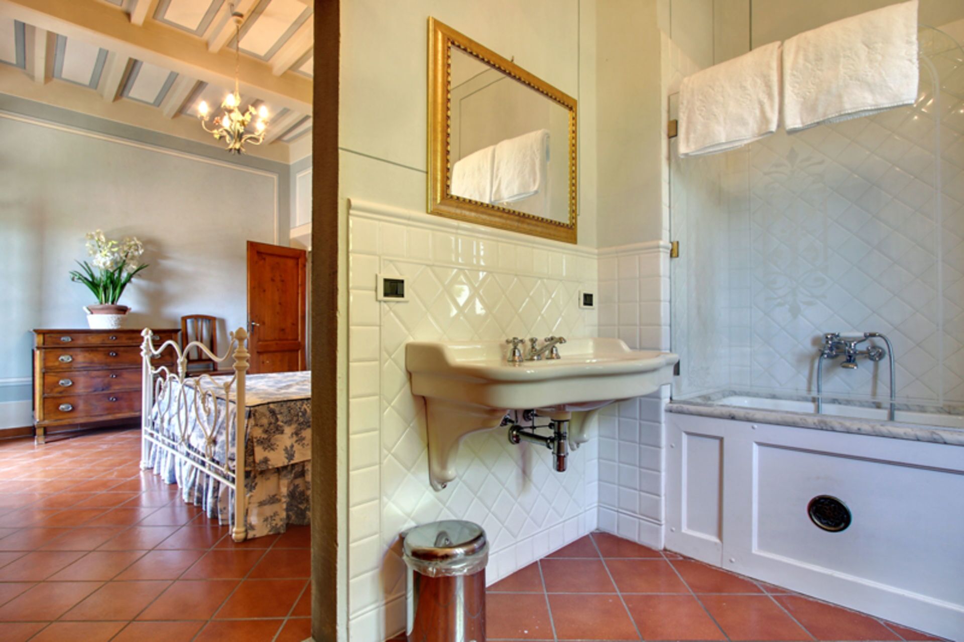 A bathroom with a white sink, a mirror, and a bathtub. There is a potted plant and a wooden dresser in the room.