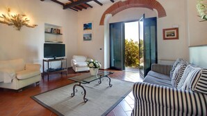 A living room with a white sofa, a striped sofa, a coffee table, a TV, and a bookshelf. There is a glass door leading outside.