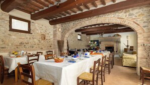 Un comedor rústico con paredes de piedra, vigas de madera y una larga mesa dispuesta para una comida.