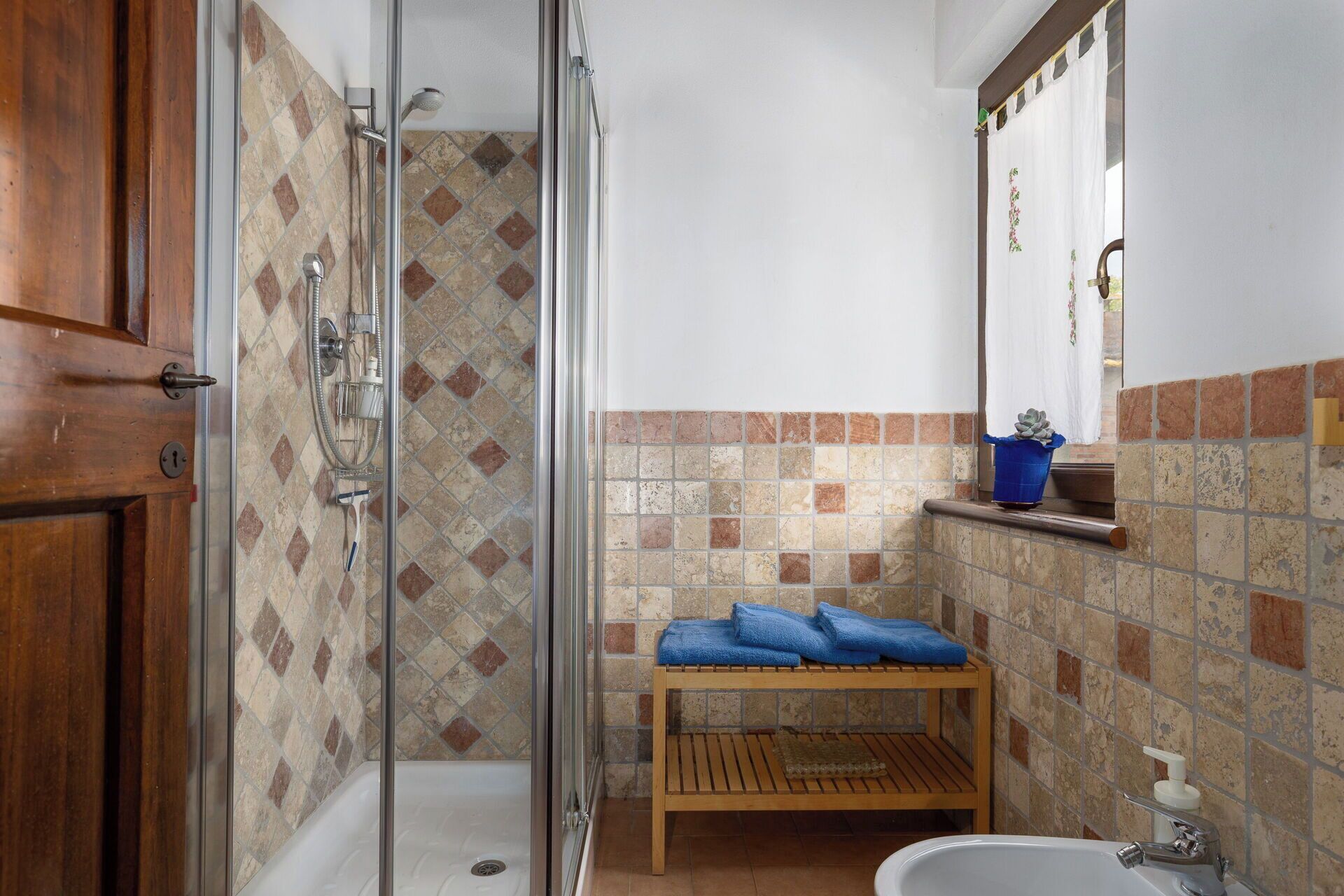 A bathroom with a shower, a sink, a wooden bench, and a potted plant.