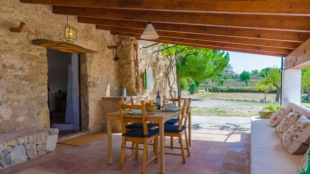 An outdoor dining area with rustic stone walls, wooden beams, and a view of a garden. - SA ROTA (DEN JOAN PORRERENC) - House with terrace in Montuïri. Free WiFi (Montuïri)