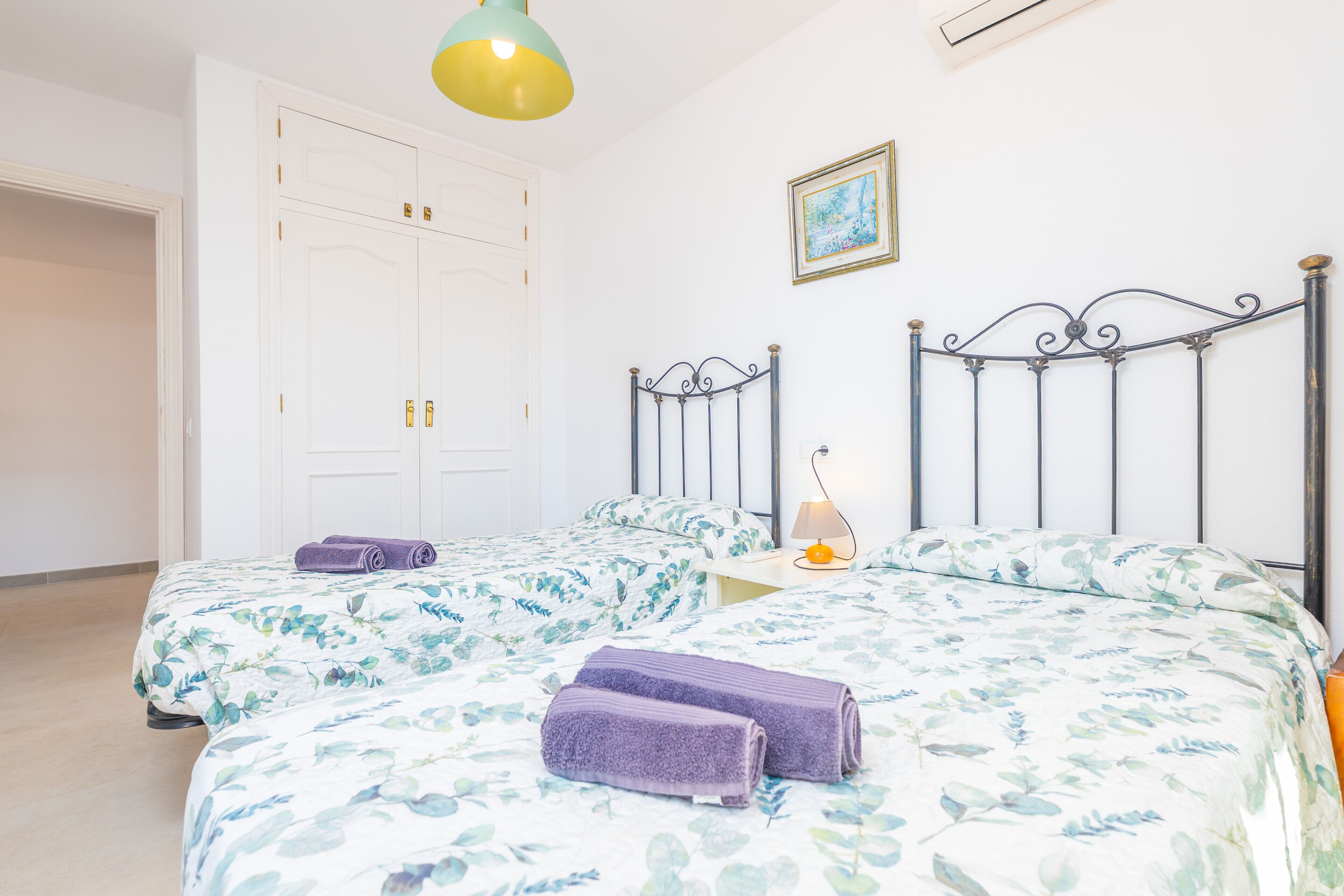 Een slaapkamer met twee bedden, een kledingkast, een nachtkastje met een lamp en een schilderij aan de muur.