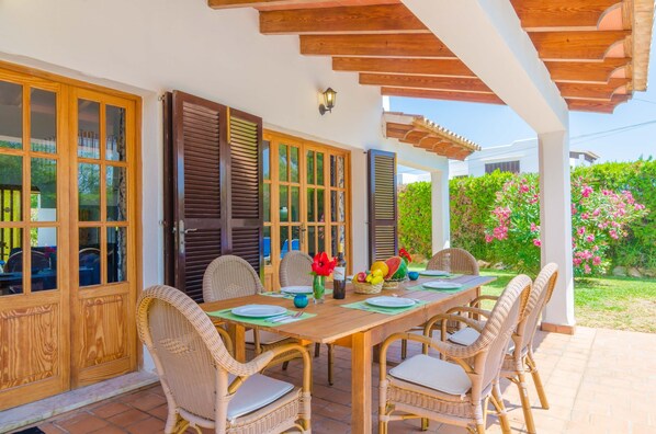 An outdoor dining area with a wooden table and wicker chairs, surrounded by wooden doors and a pergola.
