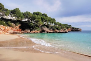 Una playa con agua turquesa cristalina, orilla de arena y acantilados rocosos con árboles.