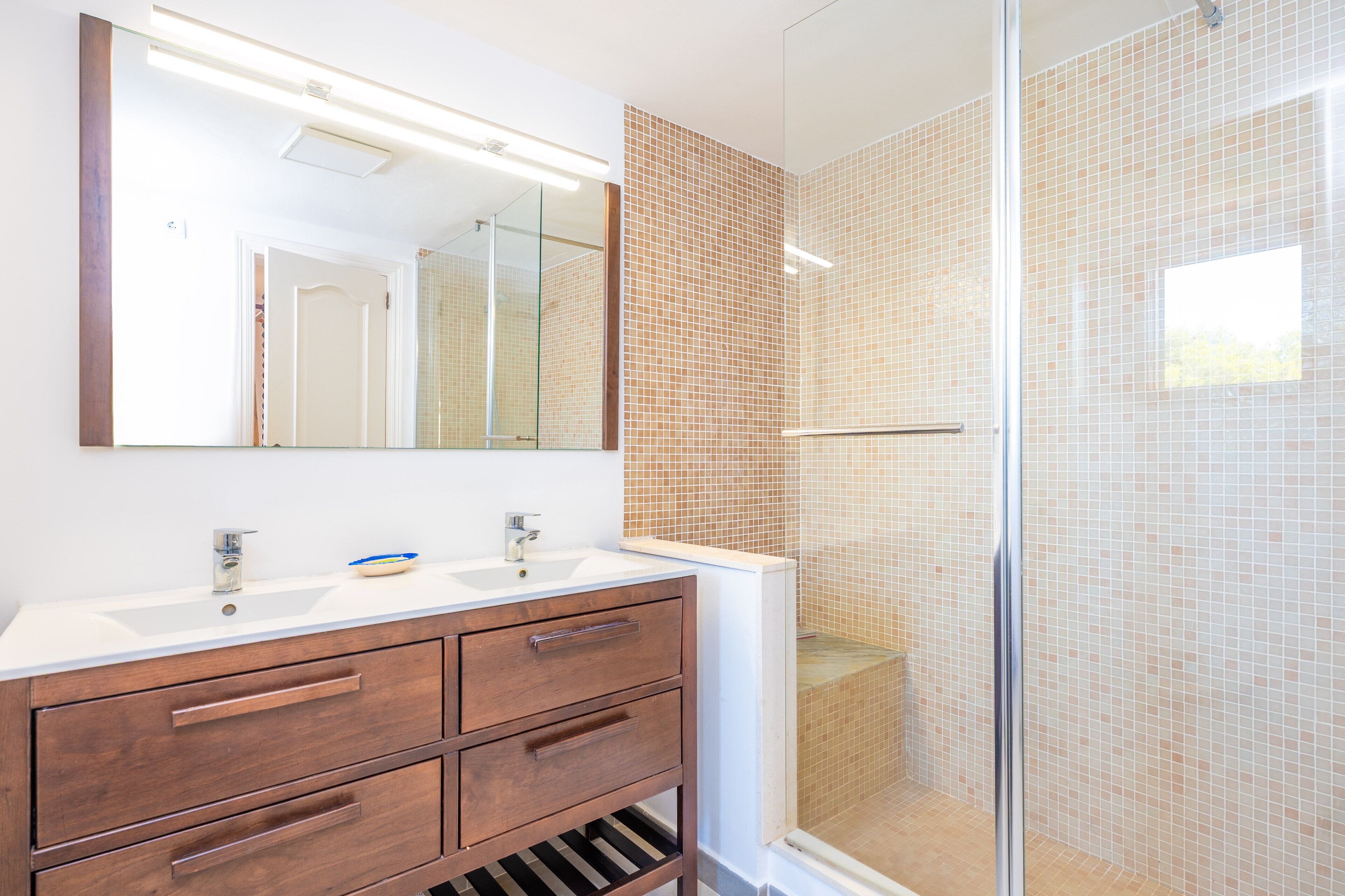 Un baño con lavamanos blanco, tocador de madera y cabina de ducha de vidrio.
