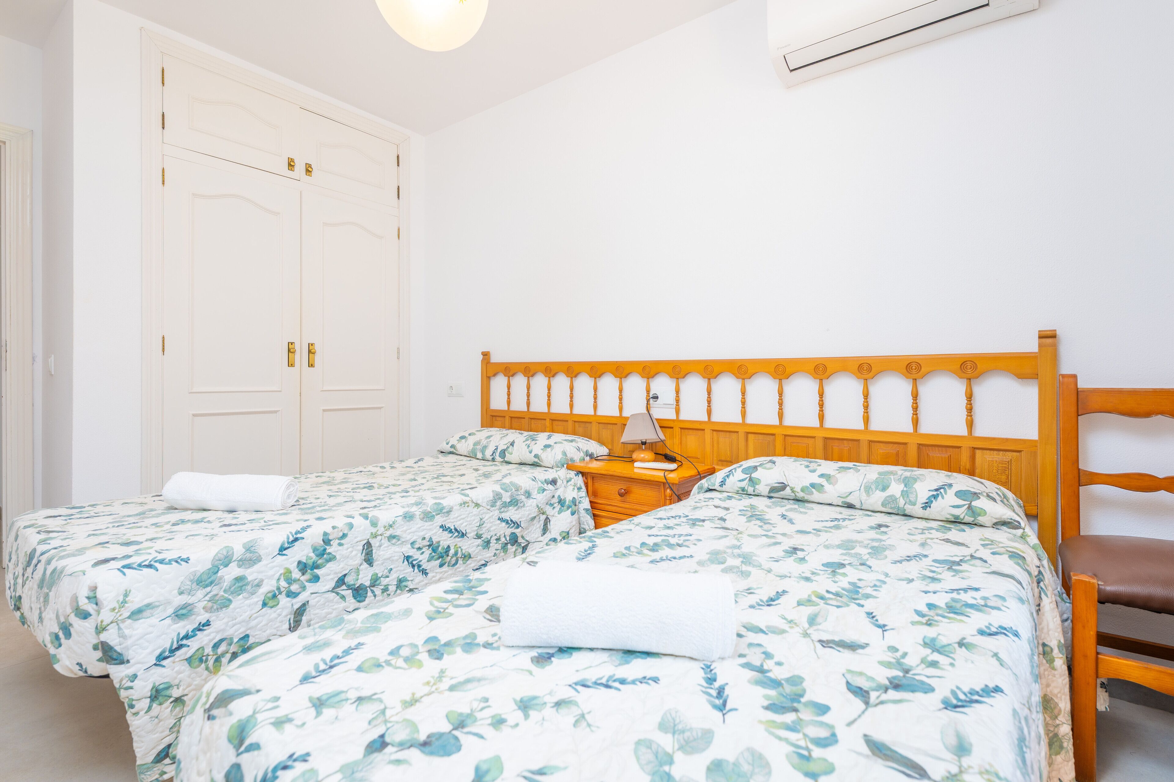 A bedroom with two beds, a wooden headboard, a nightstand, and a white wardrobe.
