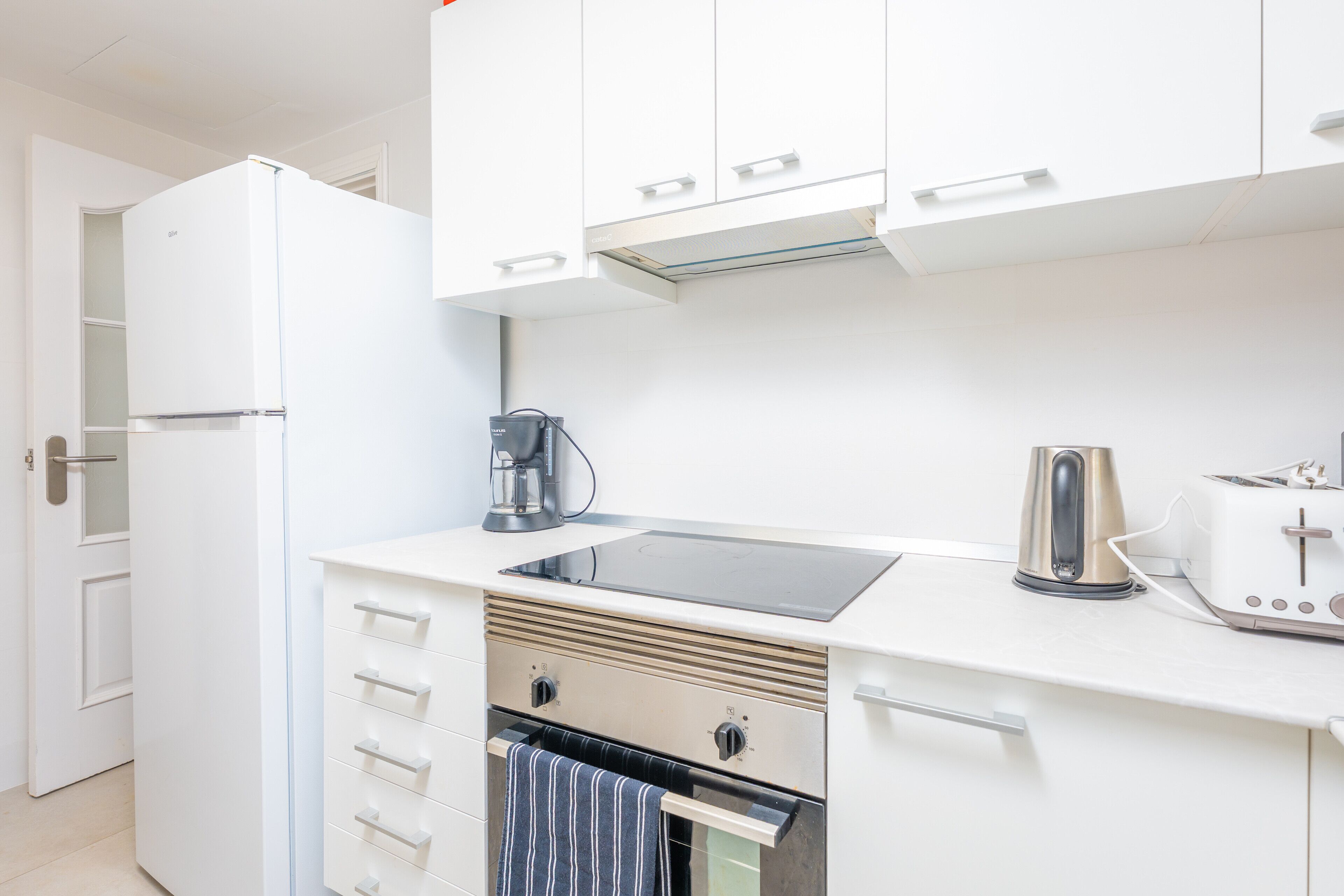Una cocina compacta con armarios blancos, horno integrado, cafetera y tostadora.