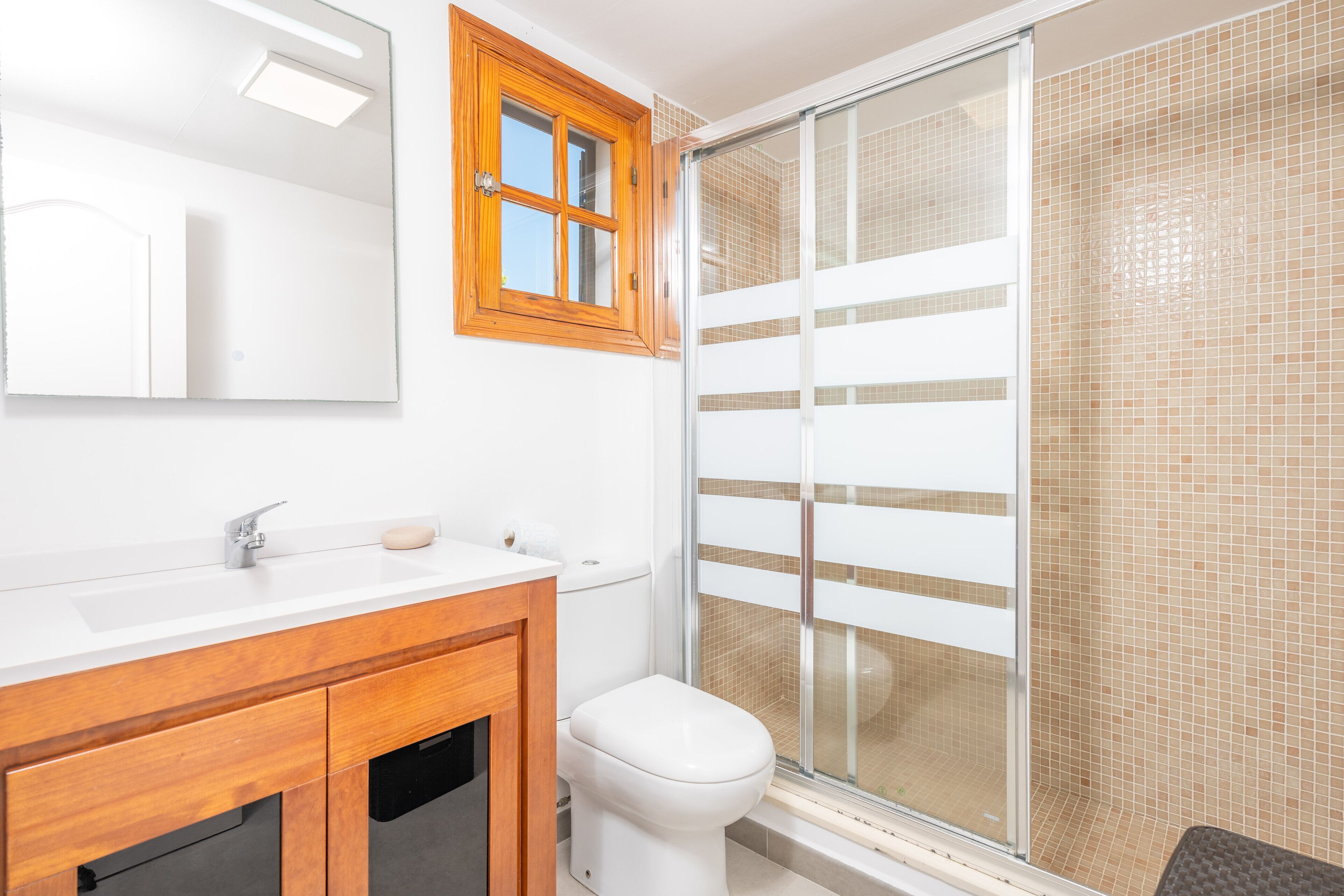 Un baño con tocador de madera, inodoro y cabina de ducha de vidrio.