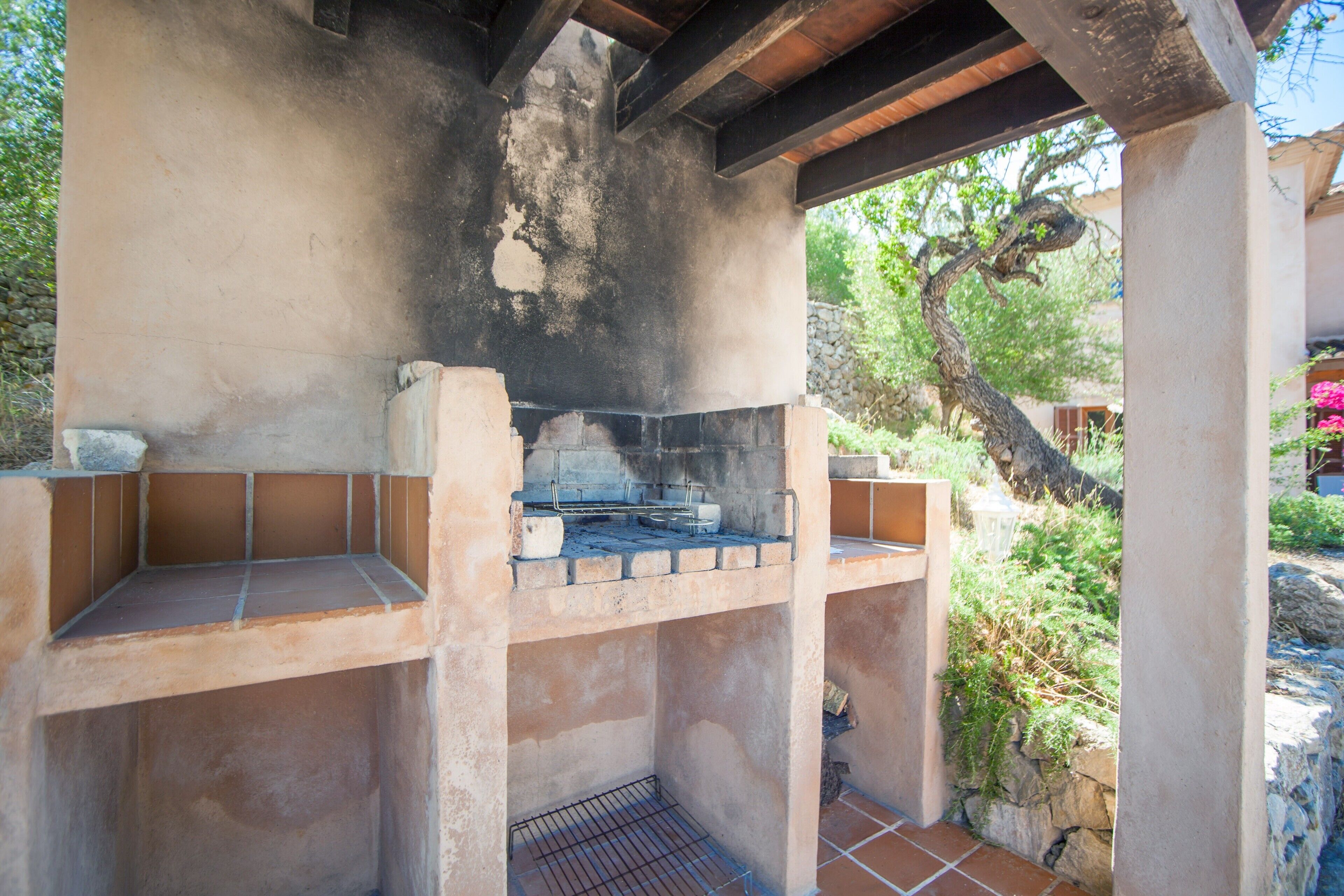 An outdoor brick oven barbecue area with a stone wall and a wooden ceiling.