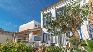 Ein zweistöckiges Gebäude mit weißer Fassade und blauen Akzenten. Ein Balkon mit einem Blumentopf und einem Stuhl ist vorhanden.