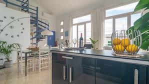 Eine moderne Küche mit schwarzer Arbeitsplatte, ein Essbereich mit weißen Stühlen und einer blauen Wendeltreppe.