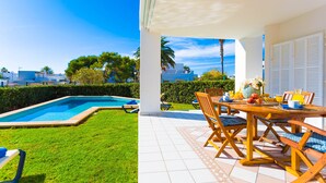 A poolside area with a dining table and chairs, a tiled patio, and a view of the pool and greenery. - SA CALETA - Villa with private pool in Cala Egos (Santanyi). Free WiFi (Santanyí)
